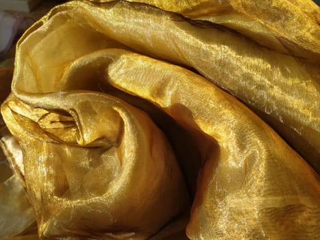 Organza is yellow-brown with a beige sheen. Shiny, reflective, beautiful fabric for curtains, tulles. Interior design option. Twisted, casually folded organza section in sunlight.
