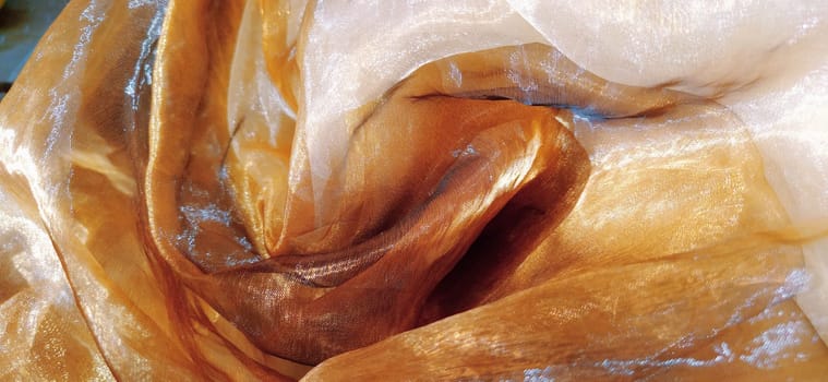 Organza is yellow-brown with a beige sheen. Shiny, reflective, beautiful fabric for curtains, tulles. Interior design option. Twisted, casually folded organza. Banner.