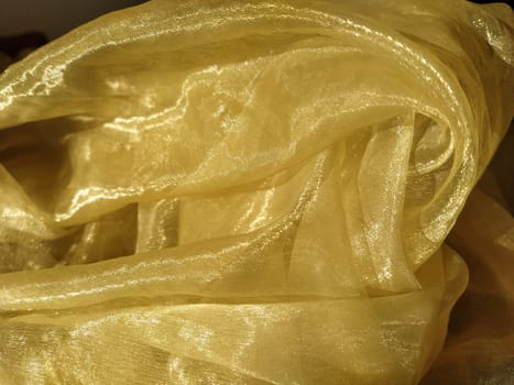 Organza is yellow-brown with a beige sheen. Shiny, reflective, beautiful fabric for curtains, tulles. Interior design option. Twisted, casually folded organza in sunlight.