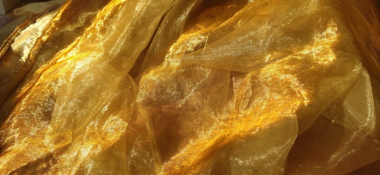 Organza is yellow-brown with a beige sheen. Shiny, reflective, beautiful fabric for curtains, tulles. Interior design option. Twisted, casually folded organza. Banner.