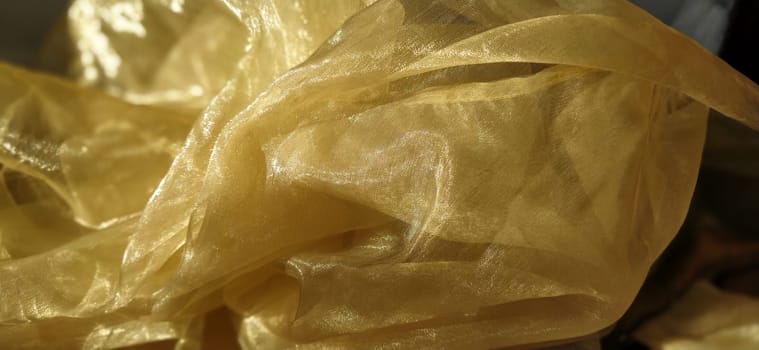 Organza is yellow-brown with a beige sheen. Shiny, reflective, beautiful fabric for curtains, tulles. Interior design option. Twisted, casually folded organza section in sunlight.