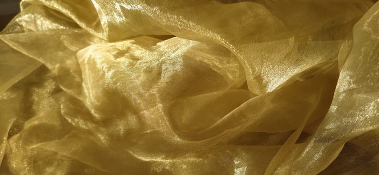 Organza is yellow-brown with a beige sheen. Shiny, reflective, beautiful fabric for curtains, tulles. Interior design option. Twisted, casually folded organza section in sunlight.