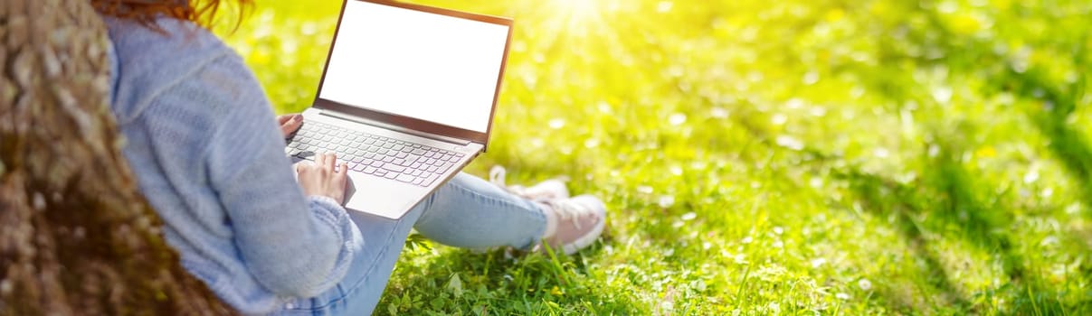 Woman with laptop sitting on the grass in the natural park. Concept of the freelance, working and learning.