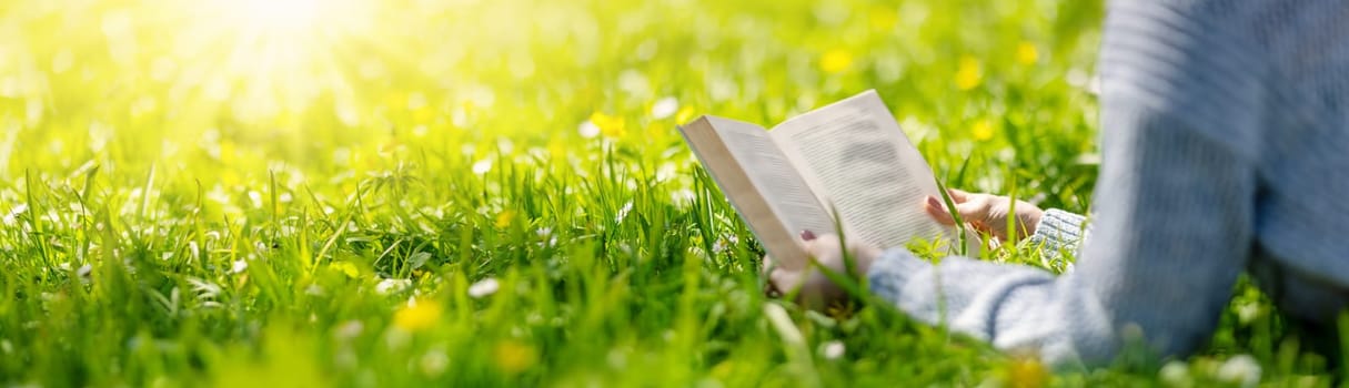 Woman lying on the blossoming meadow with book in her hands. Concept of the vacation and hobby.