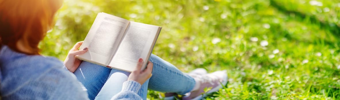 Woman sitting on the blossoming meadow with book in her hands. Concept of the vacation and hobby.