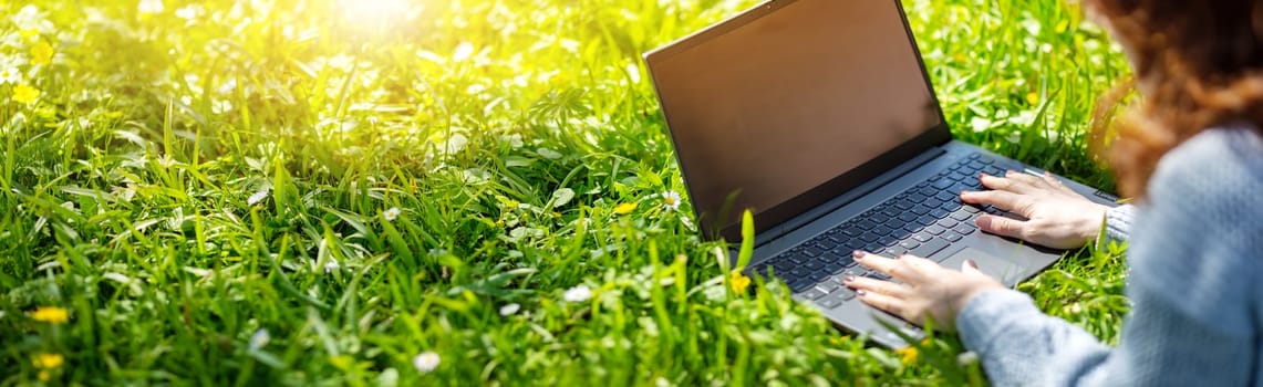 Woman lying with laptop on the blossoming meadow in natural park. Panoramic background.