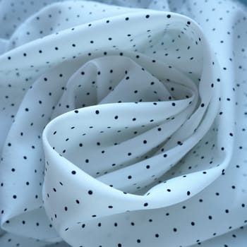 Texture of silk fabric. Black polka dots on a white background. Dress lightweight synthetic fabric in white with a repeating pattern. The textile is made up of waves and folds. Feminine classic style