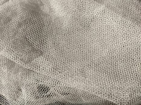 Sheer white net-like tulle. Mesh fabric wrinkled or folded carelessly. Close-up.
