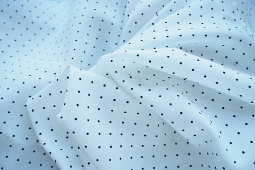 Texture of silk fabric. Black polka dots on a white background. Dress lightweight synthetic fabric in white with a repeating pattern. The textile is made up of waves and folds. Feminine classic style