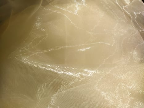 Organza in white and beige or champagne color close-up. Lightweight sheer tulle curtains under side lighting.