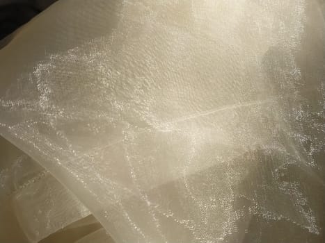 Organza in white and beige or champagne color close-up. Lightweight sheer tulle curtains under side lighting.