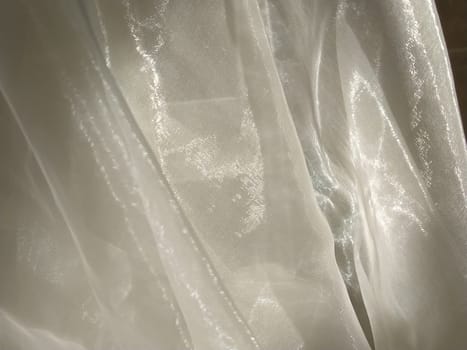 Organza in white and beige or champagne color close-up. Lightweight sheer tulle curtains under side lighting.