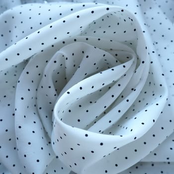 Texture of silk fabric. Black polka dots on a white background. Dress lightweight synthetic fabric in white with a repeating pattern. The textile is made up of waves and folds. Feminine classic style