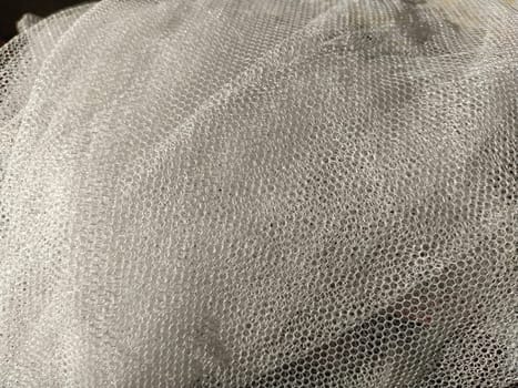 Sheer white net-like tulle. Mesh fabric wrinkled or folded carelessly. Close-up.