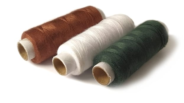 Bobbins and spools of thread of different colors - brown, white and green. Close-up. Natural light on the left side. Isolate on a white background with a light shadow. Skeins of thread. Sewing supplies. Textile production