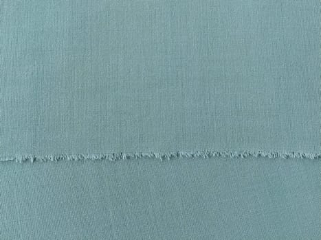 Ripped edge of fine woolen fabric in green or blue. Loose threads at the edge of a piece of textile. Close-up. Woven background. Calm green pastel color.