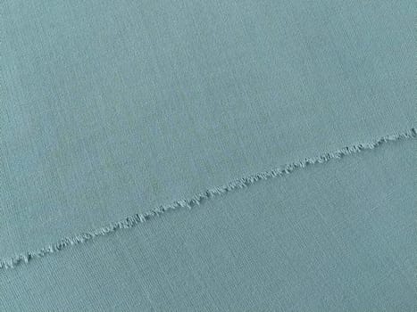 Ripped edge of fine woolen fabric in green or blue. Loose threads at the edge of a piece of textile. Close-up. Woven background. Calm green pastel color.