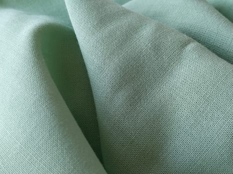 Close up of a woolen fabric of green color. Abstract canvas background, empty template. Thin natural fabric, wool or linen.