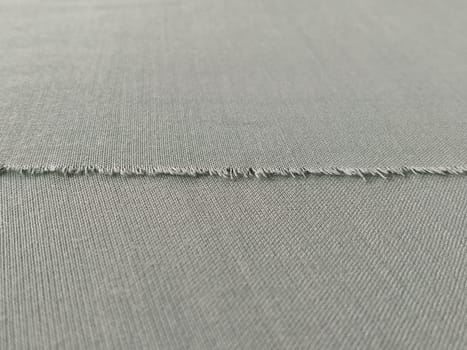 Ripped edge of fine woolen fabric in green or blue. Loose threads at the edge of a piece of textile. Close-up. Woven background. Calm green pastel color.