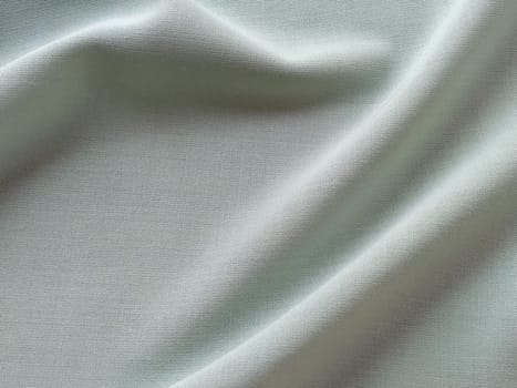 Beautifully folded light green fabric. Soft pleasant waves and flounces on textiles. Close-up. Drapery for curtains, fabric for dressmaking or upholstery.