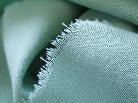 Close up of a woolen fabric of green color. Abstract canvas background, empty template. Thin natural fabric, wool or linen. The edge of the fabric is treated against chapping.