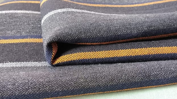 Light green and black-gray folded fabric with orange and dark blue stripes. Interior decoration. Dress fabrics in casual style. Dense material for indoor curtains and furniture finishing.