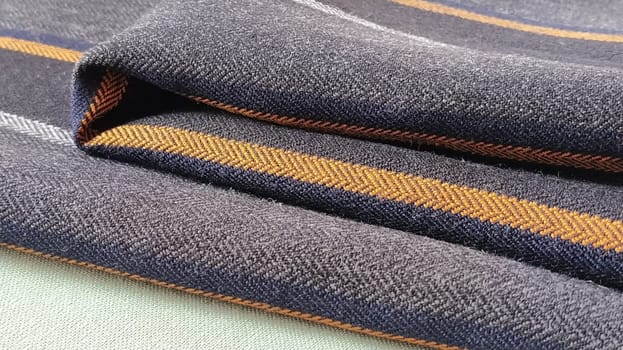 Gray-black fabric with orange and blue stripes. Textile fabric folded neatly on the surface. Natural wool material for sewing clothes and upholstery. Lifestyle. Close-up. Soft focus.