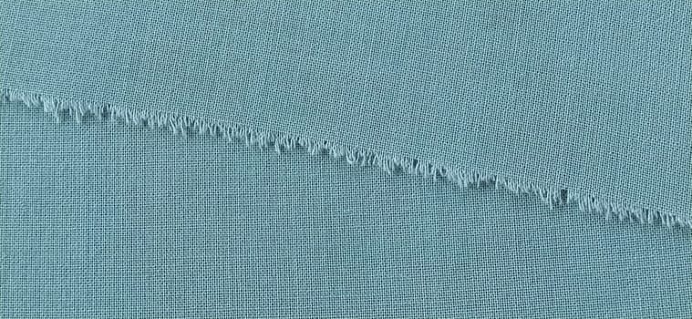 Ripped edge of fine woolen fabric in green or blue. Loose threads at the edge of a piece of textile. Close-up. Woven background. Calm green pastel color. Banner.