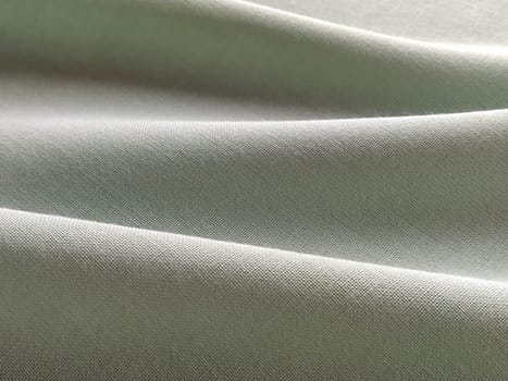 Beautifully folded light green fabric. Soft pleasant waves and flounces on textiles. Close-up. Drapery for curtains, fabric for dressmaking or upholstery.