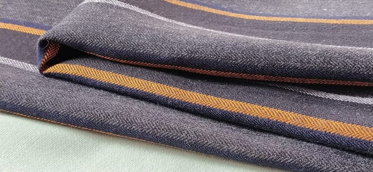 Light green and black-gray folded fabric with orange and dark blue stripes. Interior decoration. Dress fabrics in casual style. Dense material for indoor curtains and furniture finishing.