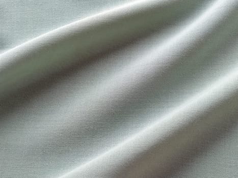 Beautifully folded light green fabric. Soft pleasant waves and flounces on textiles. Close-up. Drapery for curtains, fabric for dressmaking or upholstery.