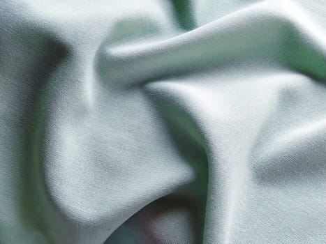 Beautifully folded light green fabric. Soft pleasant waves and flounces on textiles. Close-up. Drapery for curtains, fabric for dressmaking or upholstery.