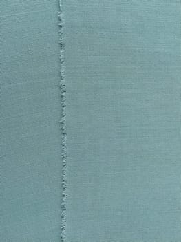 Ripped edge of fine woolen fabric in green or blue. Loose threads at the edge of a piece of textile. Close-up. Woven background. Calm green pastel color.