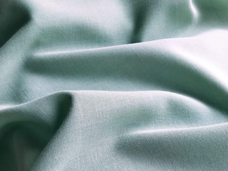 Beautifully folded light green fabric. Soft pleasant waves and flounces on textiles. Close-up. Drapery for curtains, fabric for dressmaking or upholstery.