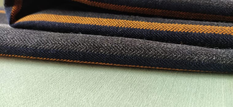Light green and black-gray folded fabric with orange and dark blue stripes. Interior decoration. Dress fabrics in casual style. Dense material for indoor curtains and furniture finishing.