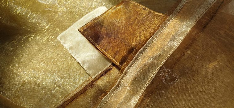 Curtain loops. Beautiful gold fabric. Organza in yellow, orange, beige and brown shades. Pleats in the fabric. Shiny gradient under the light. Folded silky tulle. Transparent curtain material. Banner.