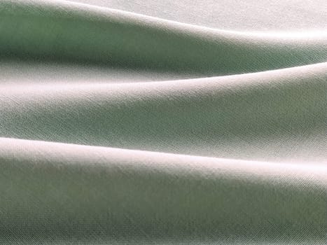 Beautifully folded light green fabric. Soft pleasant waves and flounces on textiles. Close-up. Drapery for curtains, fabric for dressmaking or upholstery.