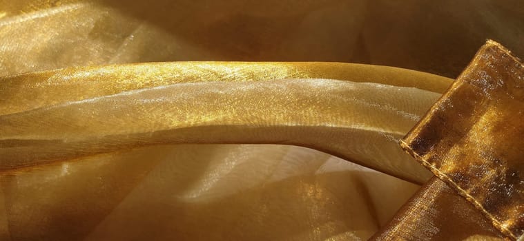 Beautiful gold fabric. Organza in yellow, orange, beige and brown shades. Pleats in the fabric. Shiny gradient under the light. Folded silky tulle. Transparent curtain material.