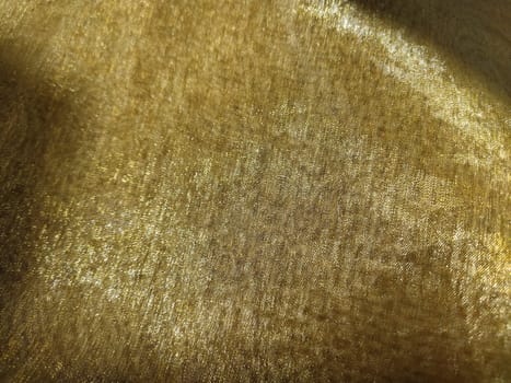 Beautiful gold fabric. Organza in yellow, orange, beige and brown shades. Pleats in the fabric. Shiny gradient under the light. Folded silky tulle. Transparent curtain material.