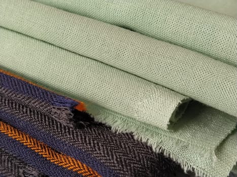 Light green and black-gray folded fabric with orange and dark blue stripes. Interior decoration. Dress fabrics in casual style. Dense material for indoor curtains and furniture finishing.