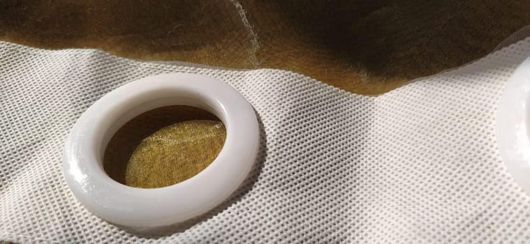 Plastic rings for attaching the fabric to the curtain rod. White plastic organza tulle eyelets. Light curtain in beige, brown or orange colors. White non-woven fabric. Finished textile edge. Interior element