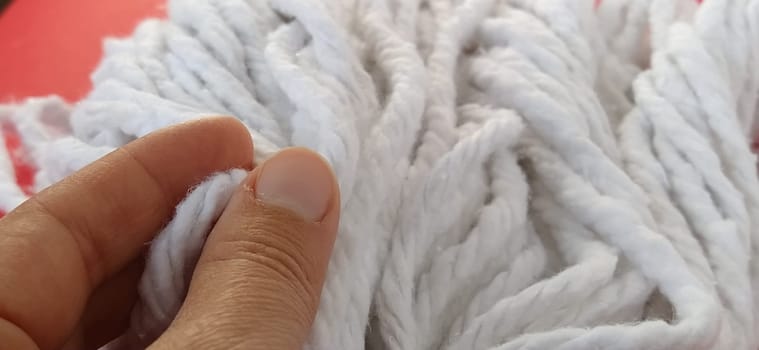 A woman's hand touches the cotton threads of the mop head. Choosing a mop for cleaning. Household cleaning work. White ropes. Cleaning lady's fingers