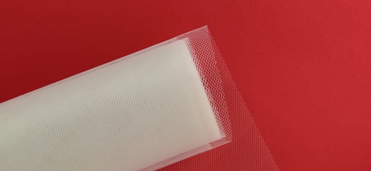 Fabric - white mesh in a roll on a red background. Nylon tape for tying bows on hair. A skein of tulle fabric. Copy space.