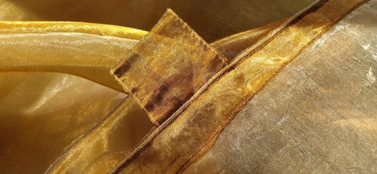 Curtain loops. Beautiful gold fabric. Organza in yellow, orange, beige and brown shades. Pleats in the fabric. Shiny gradient under the light. Folded silky tulle. Transparent curtain material. Banner