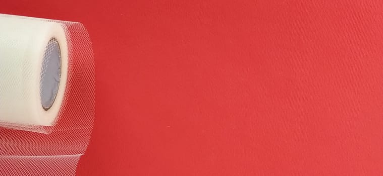 Fabric - white mesh in a roll on a red background. Nylon tape for tying bows on hair. A skein of tulle fabric. Copy space.
