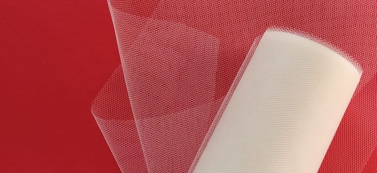 Fabric - white mesh in a roll on a red background. Nylon tape for tying bows on hair. A skein of tulle fabric. Copy space.