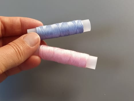 Spools of pink and blue thread on a woman's hand. Textile industry. Gray background.