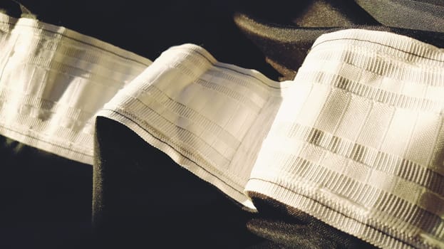 Curtain tape on black curtains. A wide white stripe - a tape for hanging curtains by hooks to the cornice. Home interior. Apartment decor. Light industry.