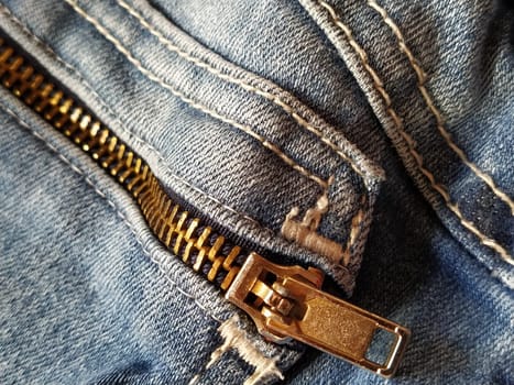 Denim fabric with seams made with red or beige threads close-up. Textile texture. Rough metal zip lock. Sewn-on pocket. Blue color of the material. Light industry sewing product