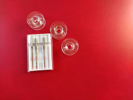plastic bobbins and a set of sewing machine needles on a red background.